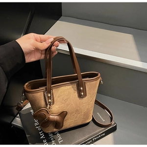 Detail of vintage brown tote bag with dog charm and detachable strap on stone steps