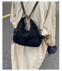 Detail view of black matte backpack with gold zippers worn over a beige trench coat
