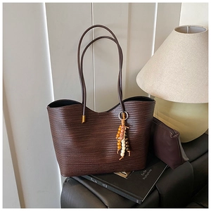 Détail du sac cabas tressé marron foncé avec pochette en cuir et pendentif en bois