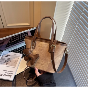 Detail of a brown textured tote bag featuring M'Dolan logo, long strap and bear pendant