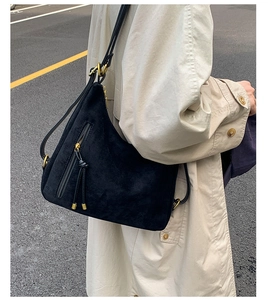 Detail view of black suede shoulder bag with gold zipper and stylish tassel on beige trench