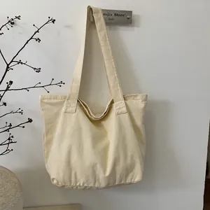 Close-up of cream canvas tote bag with wide shoulder straps hanging in a minimalist setting