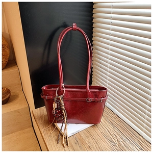 Close-up of a burgundy glossy shoulder bag with leather buckle and heart tassel charms
