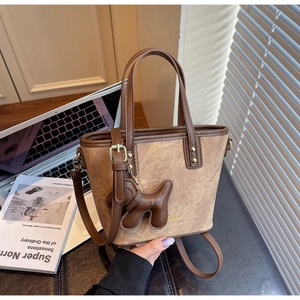 Detailed view of beige textured crossbody bucket bag with brown trim and puppy charm