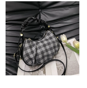 Close-up of checkered crossbody bag with ruffle handle and gold hardware on black background