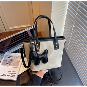 Detail of crossbody bucket bag with black leather trim and cute puppy charm accessory