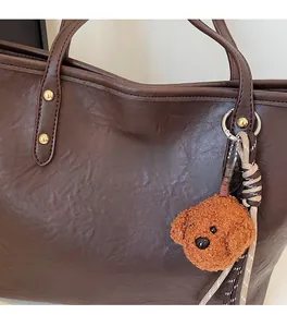 Close-up of dark brown tote bag featuring gold studs and a plush teddy bear charm