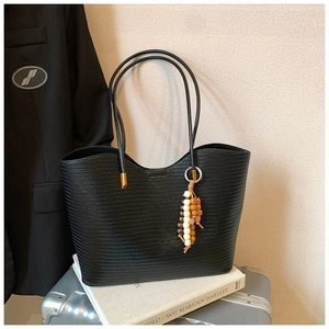 Détail d'un sac cabas noir tissé avec pendentif en perles et fines anses élégantes
