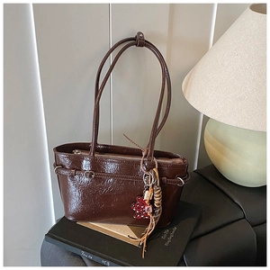 Detailed macro of dark brown glossy patent leather shoulder bag with a leopard bear charm