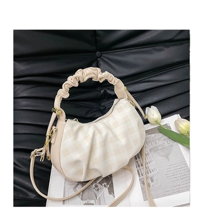 Detail of beige checkered dumpling bag with pleated handle on a black leather background