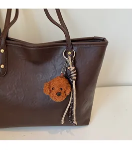 Close-up of a dark coffee tote bag featuring a teddy dog charm and gold logo plate