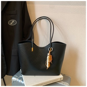 Détail du sac cabas tressé noir avec pampille de perles sur une valise de voyage