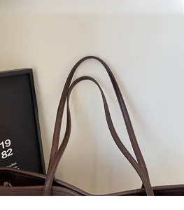 Detailed close-up of slim dark brown leather shoulder straps on a large tote bag