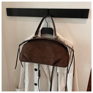 Close-up of brown suede handbag with embossed logo detail on a minimalist coat backdrop