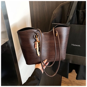 Détail du grand sac cabas tressé marron foncé avec de longues anses et breloque