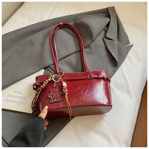Close-up of deep red glossy shoulder bag with a cute bear charm on a grey blazer