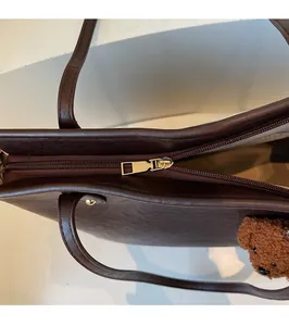 Close-up of golden zipper hardware and brown faux leather texture on tote bag