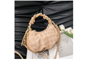 Detail of apricot checkered dumpling bag with pleated handle on a black leather background