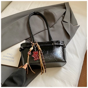 Detail of black glossy leather bucket bag with leopard heart charm and woven tassel