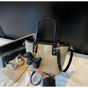 Detail of crossbody bucket bag with beige fabric, black leather trim, and puppy charm