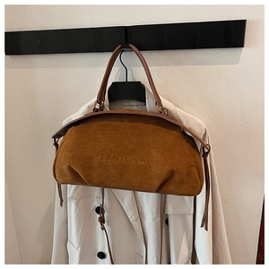 Detail of brown suede tote bag with embossed brand logo on a coat rack