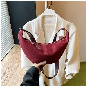 Detailed texture of burgundy suede crescent bag with silver zipper and leather strap