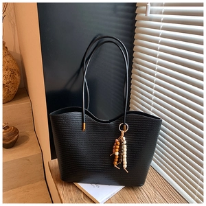 Détail du grand sac cabas noir tissé avec pendentif à pampilles sur une table en bois