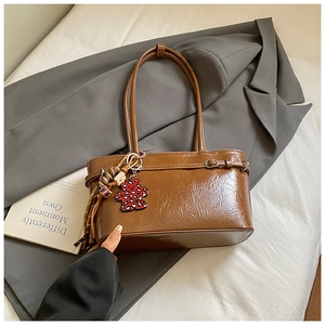 Detail of caramel leather shoulder bag with bear charm on grey blazer backdrop
