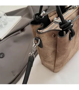 Dettaglio borsa in tela marrone con manico in pelle nera annodato e minuterie metalliche