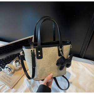 Detail of grey suede tote bag with black leather handles and M.Daim logo and ribbon