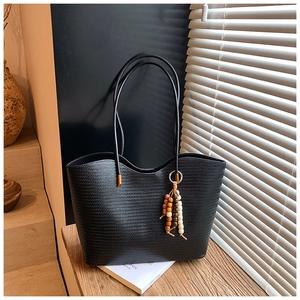 Détail d'un grand sac cabas noir tressé avec fines lanières et pompons en perles de bois