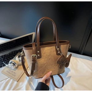 Detail of a brown canvas bucket bag with leather trim and cute bear charm on a desk