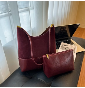 Détail du grand sac cabas en daim bordeaux et sa pochette assortie sur un bureau chic