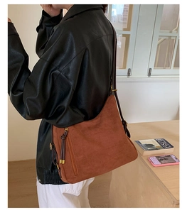 Close-up of brown suede shoulder bag featuring a vertical zipper pocket and leather puller