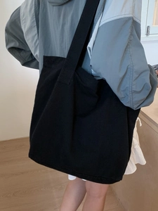 Black canvas tote bag with large capacity shown in a minimalist home setting on a model