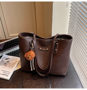 Detail of dark brown tote bag featuring textured leather and a cute plush bear charm