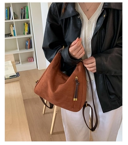 Close-up of brown matte hobo bag with vertical zipper and tassel detail on model
