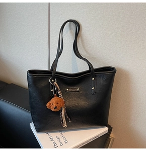 Detail of retro black PU leather tote bag with metallic logo and cute teddy bear charm