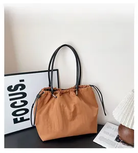 Detail of caramel drawstring tote bag with black leather straps on a modern desk