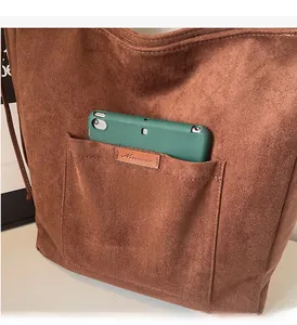 Detail of durable front pocket on brown suede tote bag holding a green tablet