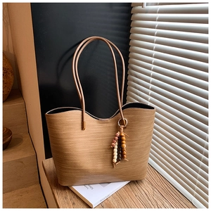 Gros plan du sac fourre-tout tressé marron clair avec détail de pompon à perles