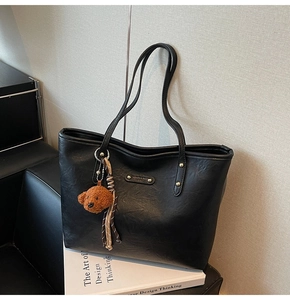 Detail of black leather tote bag with metallic logo plate and puppy charm decoration