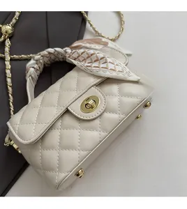 Détail d'un sac matelassé crème avec chaîne dorée et poignée décorée d'un foulard en soie
