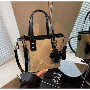 Detail of beige suede bucket bag with black leather handle and a dog-shaped charm