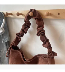 Detail view of a brown suede hobo bag featuring a distinctive ruched handle and metal zipper