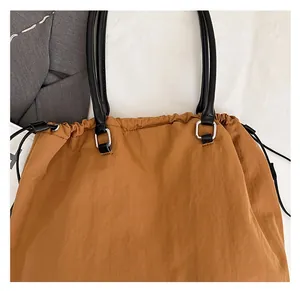 Detail of tan fabric tote bag with drawstring closure and black leather strap
