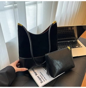 Détail du grand sac cabas en daim noir et de sa pochette assortie sur un bureau chic