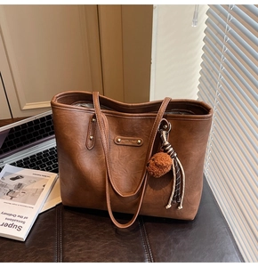 Close-up of brown PU leather tote bag with gold logo plate and cute bear charm detail