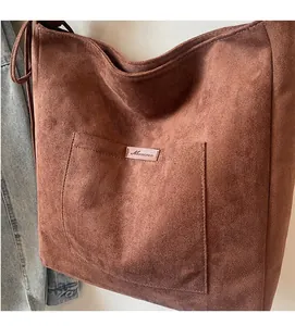 Detail of dark brown tote bag with large front pocket and pink logo label on suede fabric