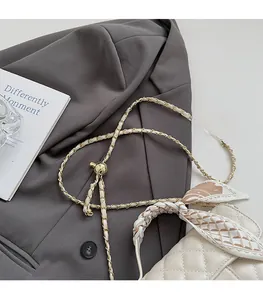 Close-up of quilted cream crossbody bag with woven gold chain and decorative silk scarf
